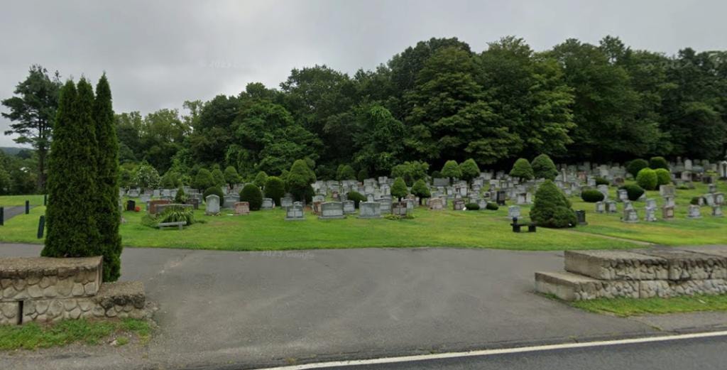 Hebrew Benefit Cemetery grounds with manicured shrubs, gravestones, and lush tree line