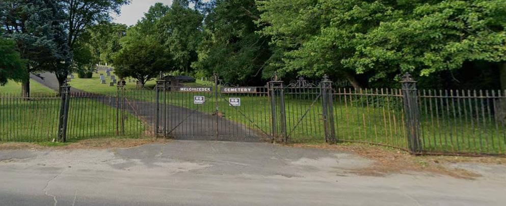 Melchi Zedek Cemetery entrance with ornate iron gate and gravestones on a green hillside