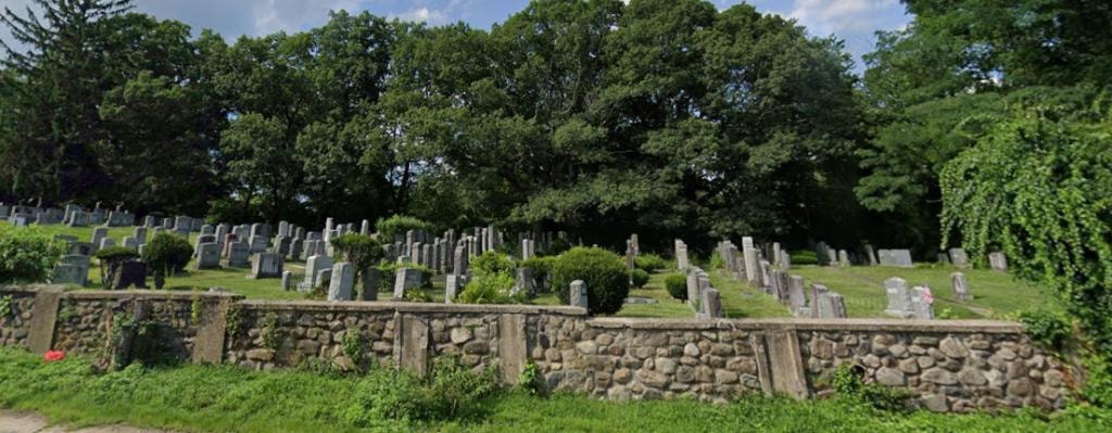 Sharis Israel Cemetery grounds with stone wall and gravestones among lush trees